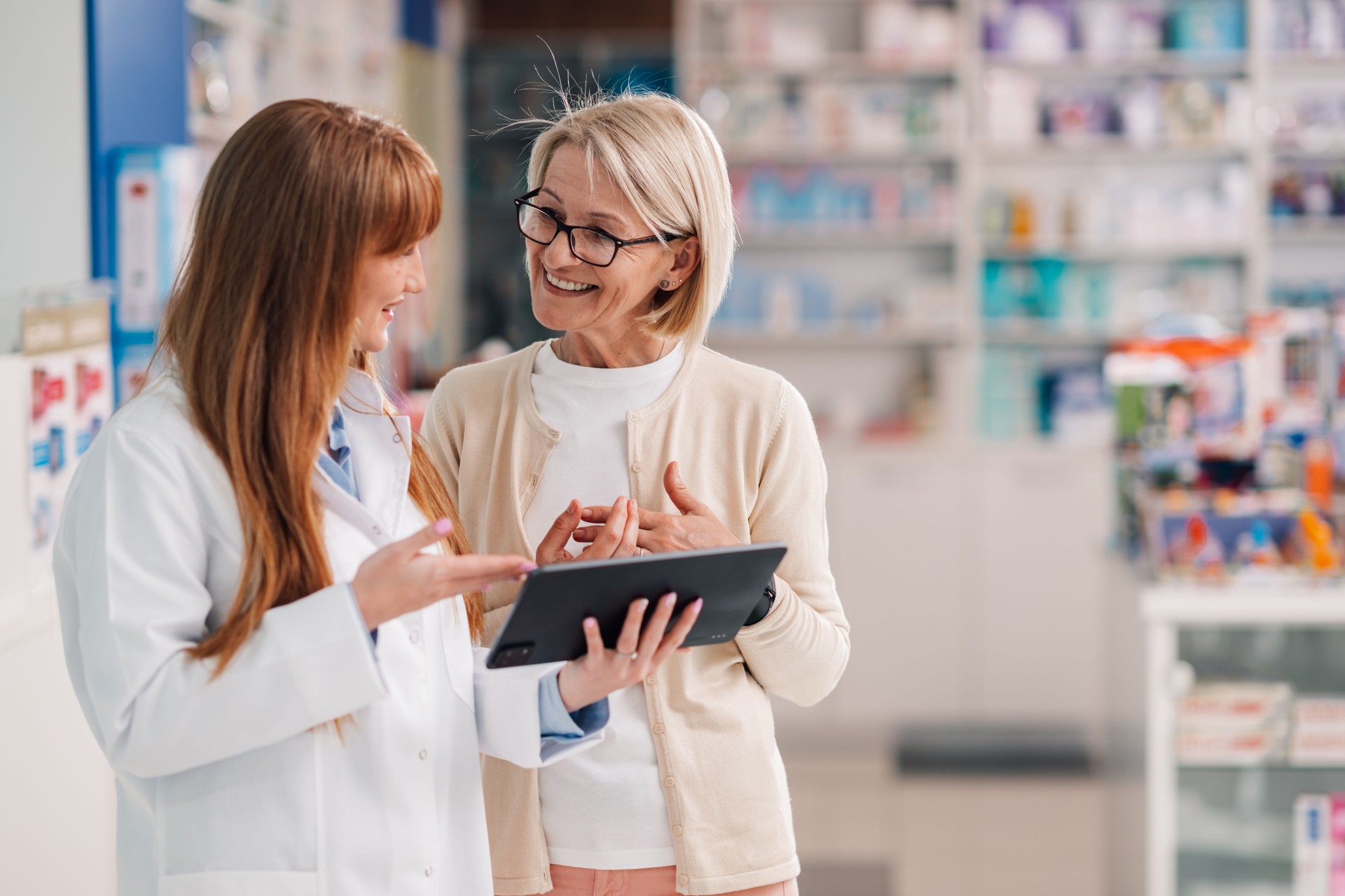 Friendly pharmacist showing information on digital tablet to customer in drugstore